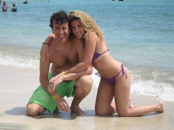 Couple crouching on wet sand, he in green shorts, she in purple bikini