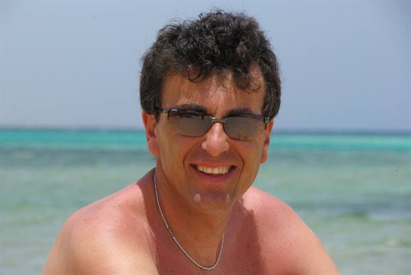 Smiling man in sunglasses with silver necklace by the turquoise sea