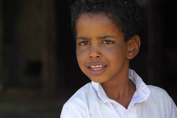 Boy in white shirt looking at camera, natural light on face