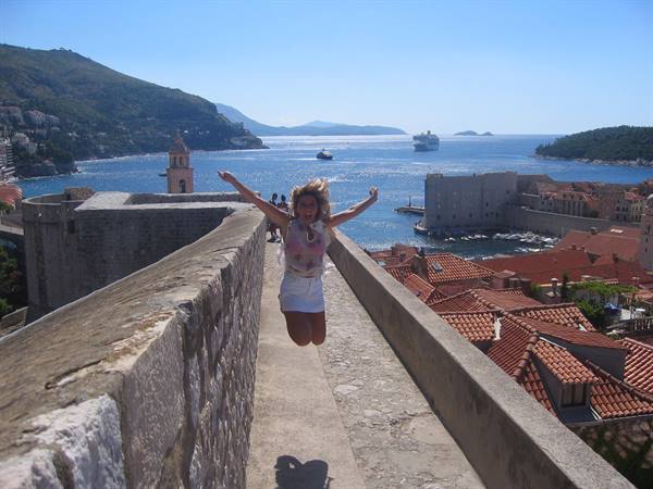 Tourist jumps joyfully atop Dubrovnik walls, red roofs and Adriatic sea