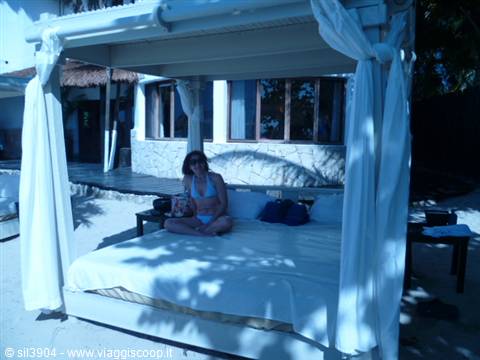Woman in bikini sitting on a white canopy daybed on a tropical beach