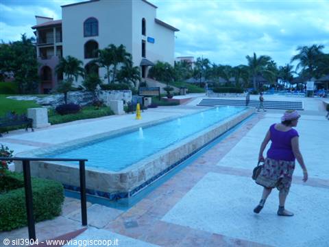 Woman walks beside a long pool at a resort with palm trees