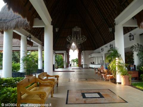 Resort lobby with thatched roof, white columns, wooden benches and wrought iron chandelier