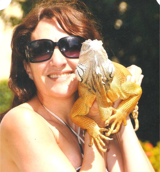 Woman in sunglasses holds a golden iguana in the sunlight
