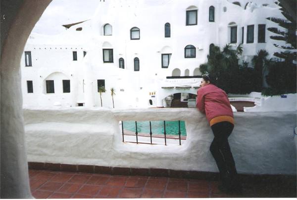 Woman leaning on Casapueblo terrace, curved white buildings and turquoise pool