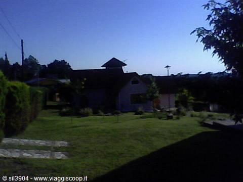 House with wooden roof and small tower amid green garden at dusk