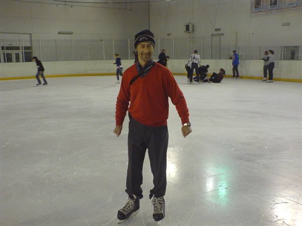 Man in red sweater and beanie skating on indoor ice rink