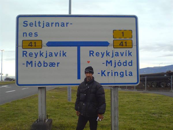 Man in black jacket beneath road sign with directions to Reykjavik