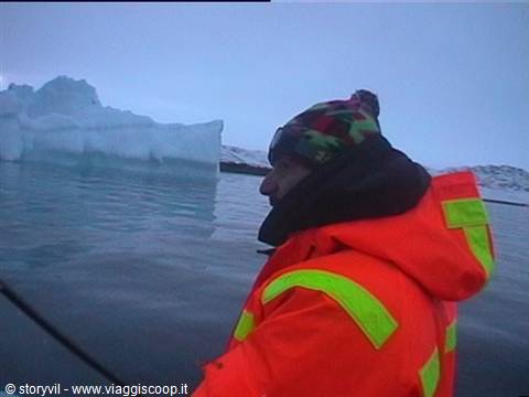 Man in fluorescent orange suit on a boat facing icebergs among sea ice