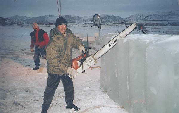 Man with a Stihl chainsaw cuts an ice block, snowy mountains behind
