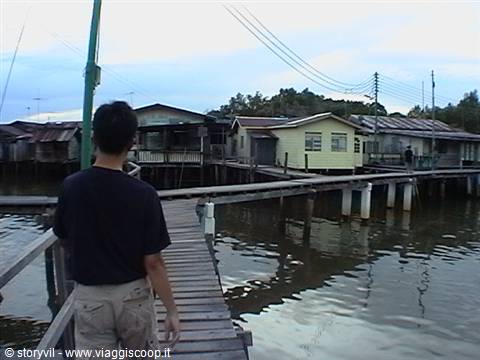 Boy walks on wooden boardwalk past stilt houses above the water
