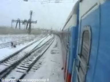 Blue train along snow-covered tracks, grey winter light