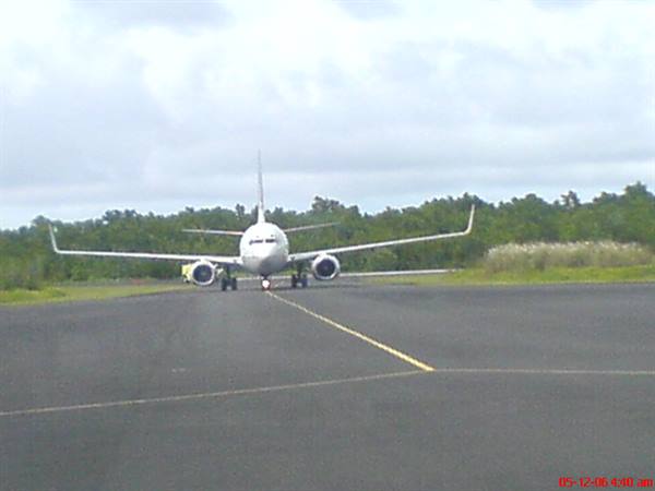 Airplane taxiing on the runway, green trees under a cloudy sky
