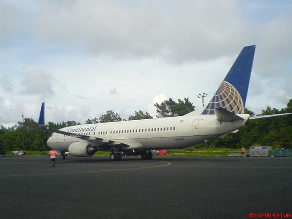 White Continental airplane with blue tail parked on tarmac, worker in orange vest walking nearby