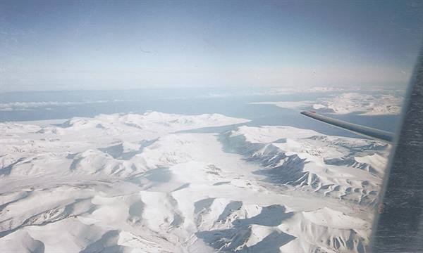 Airplane wing over snow-covered Svalbard mountains in cold light