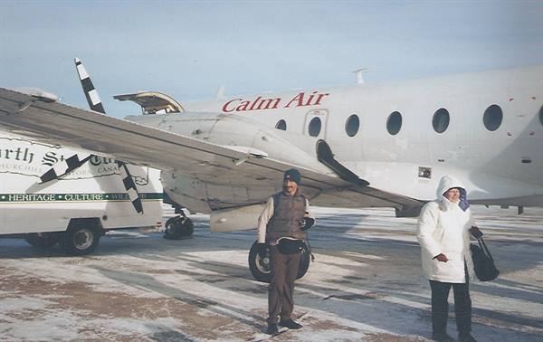 Two winter passengers beside a parked Calm Air plane on the snow
