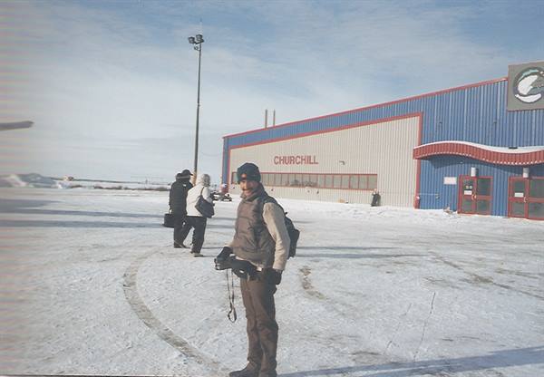 Traveler with camera in front of Churchill airport, snow and blue sky