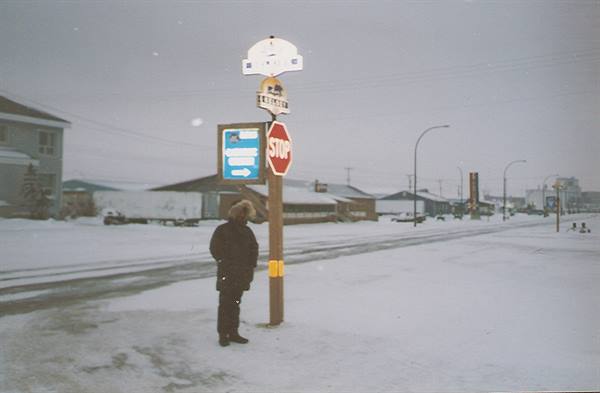 Child in hooded parka beside a stop sign pole on snowy street