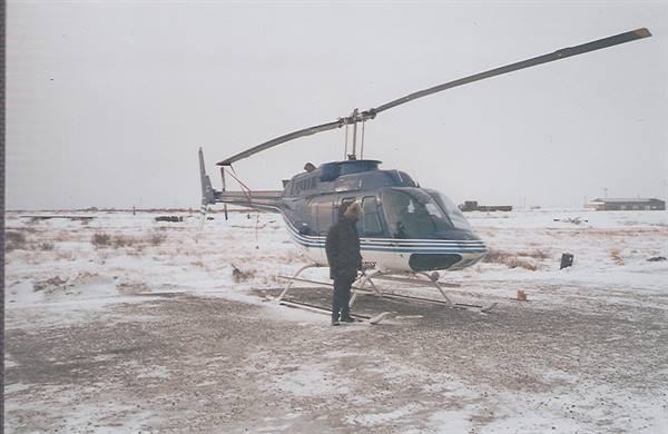 Man in coat standing beside a blue and white helicopter on snowy ground