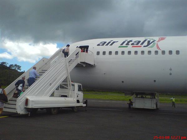 Passengers boarding an Air Italy plane via mobile stairs under cloudy skies