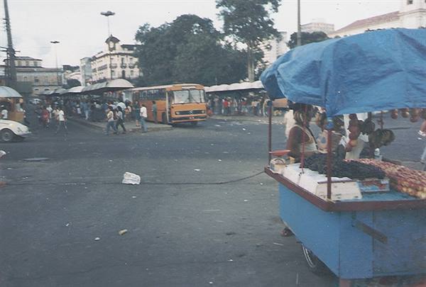 Fruit cart with blue tarp in a busy square, yellow bus approaching
