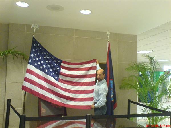 Man in blue shirt holding an American flag in a lobby with plants