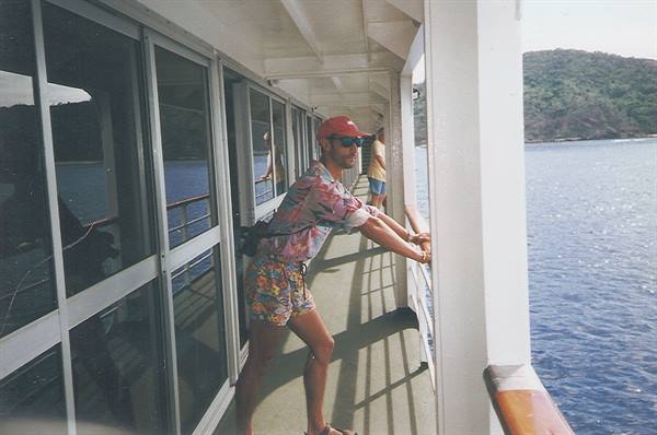 Tourist in red cap leaning on ship railing overlooking a green bay