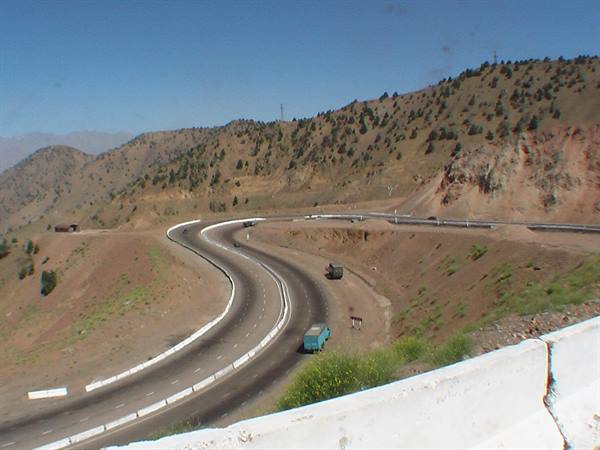 Truck drives a highway curve between dry hills and sparse bushes