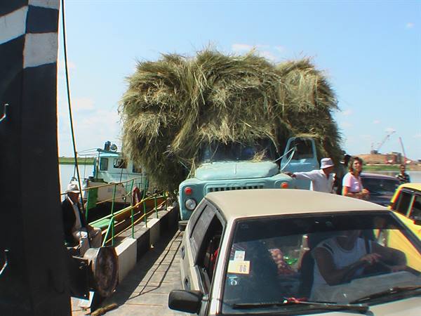 Hay-loaded truck boarding a crowded river ferry with waiting cars