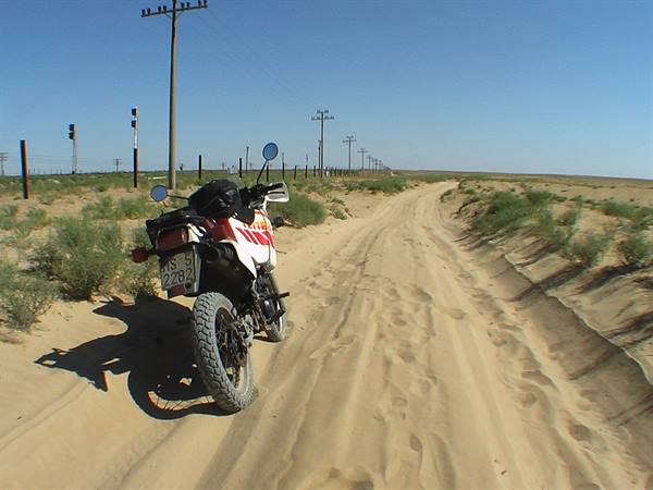 Adventure motorcycle parked on sandy desert track among shrubs under blue sky