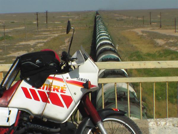 Yamaha Tenéré motorcycle parked beside a long elevated pipeline in the steppe