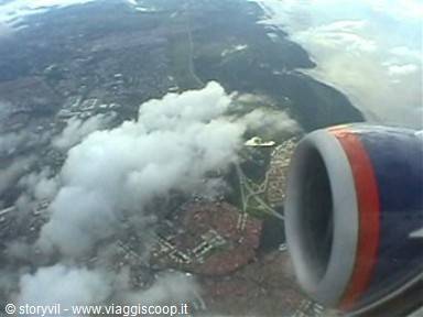 Red and blue airplane engine above clouds and coastline