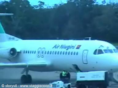 White and green Air Niugini plane parked at airport, ground crew working below