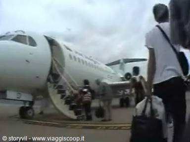 Passengers with bags boarding a plane via airstair under cloudy sky