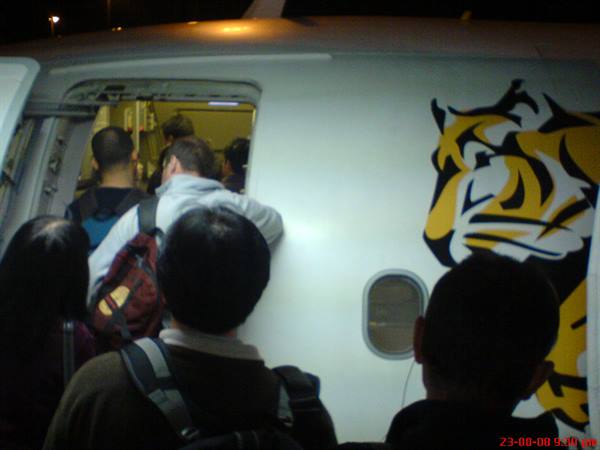 Passengers with backpacks boarding a Tigerair plane at night, yellow fuselage