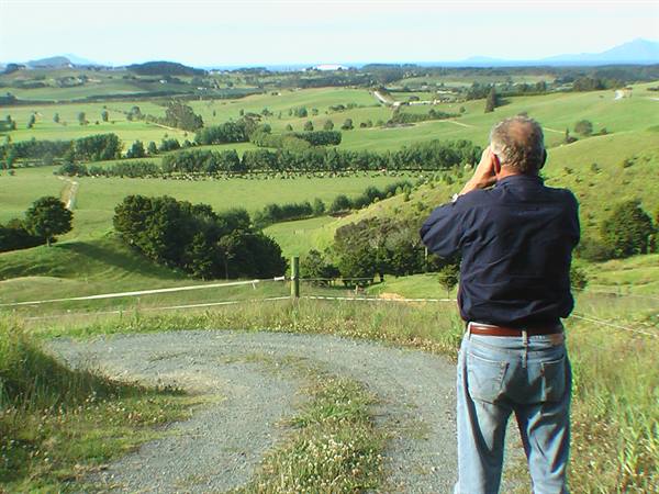 Man photographs green rolling hills and fields from gravel path