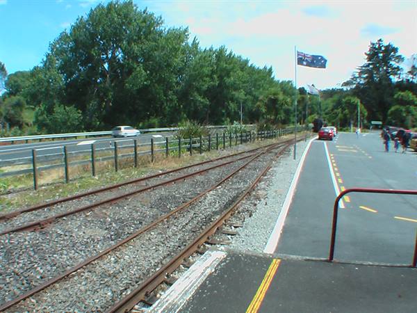 Railway track beside a road with New Zealand flag and parked cars