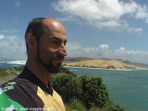 bearded man in foreground before turquoise sea and sand dunes