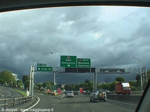 Motorway with green signs toward Helensville and Hamilton, stormy sky, moving traffic
