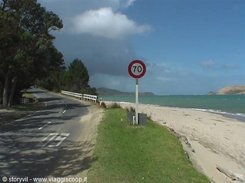 Speed limit 70 sign on coastal road, sandy beach and turquoise sea