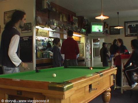 Green billiard table in a crowded pub, people at the bar with TV