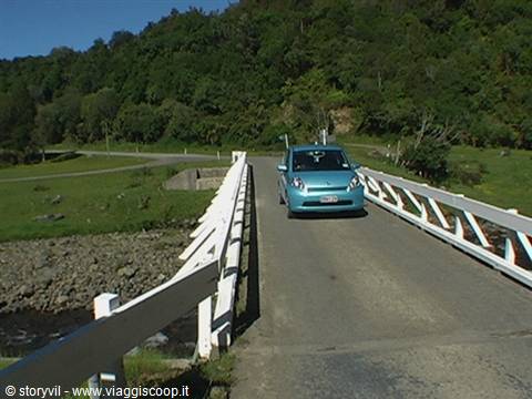 Blue car crossing wooden bridge with white railings over a river