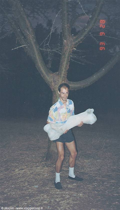 Smiling tourist holding a giant bone under a tree at night