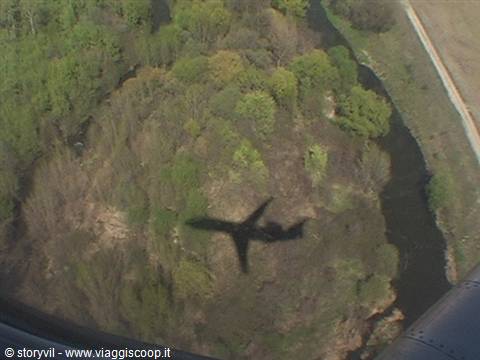 The airplane's shadow cast on woods and a winding river seen from above