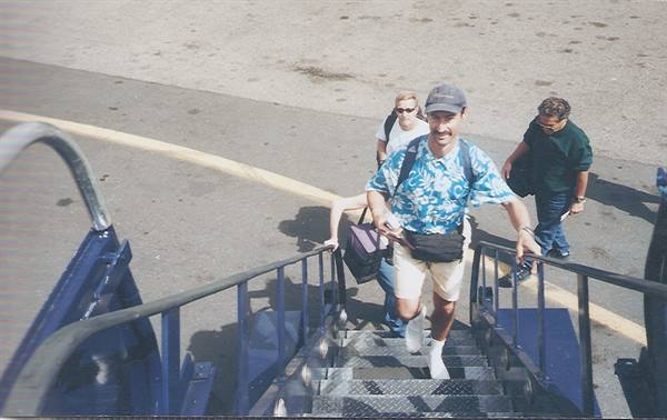 Men with backpacks climb blue metal airstairs toward the plane on the tarmac