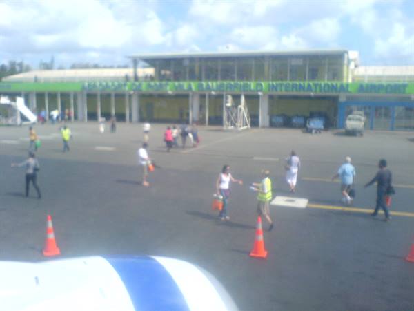 Travelers with bags walking across the tarmac toward Grantley Adams International Airport terminal