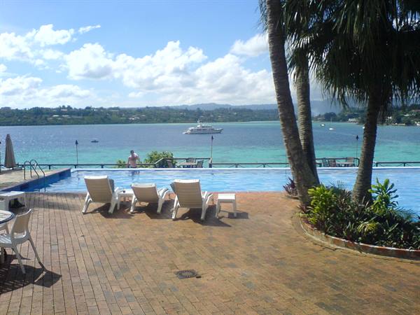 White loungers by the pool overlooking turquoise bay, yacht offshore, palm trees