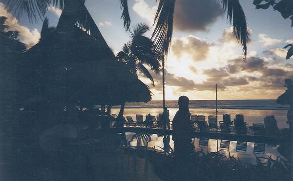 Woman's silhouette among palms and lounge chairs by the beach at dusk