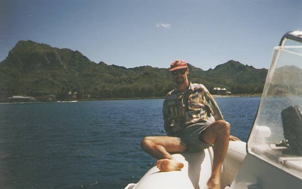 Man in red cap sitting on inflatable boat near green mountains over blue sea