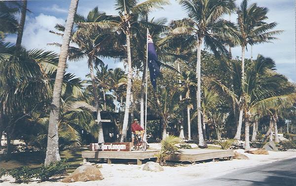 Cyclist in red shirt beside Durulong sign, flag and palm trees